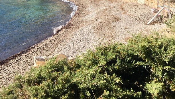 Una zona costanera amb una platja de petits cabassets, aigua cristal·lina i una tanca blanca.