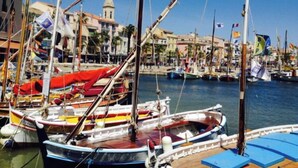 Un port esportiu amb diverses embarcacions amarrades, cel blau clar i edificis al fons.