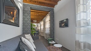 Un salon moderne avec un canapé gris, une petite table ronde et un téléviseur fixé au mur.