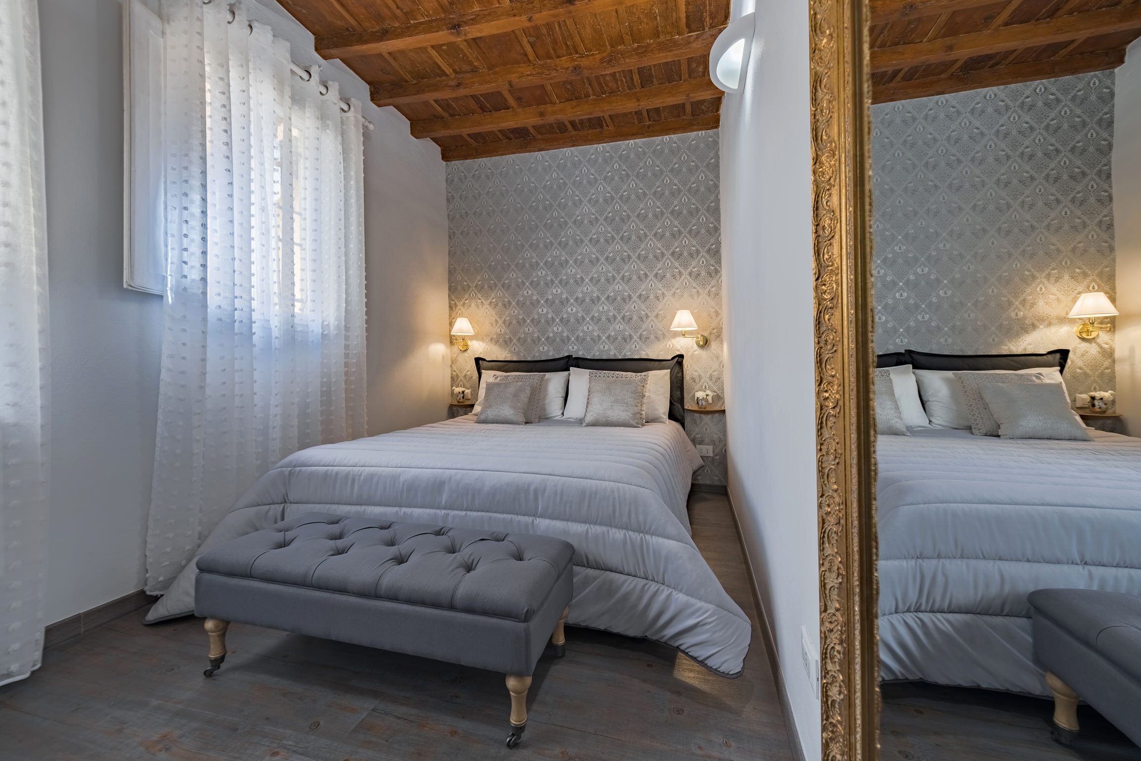 Une chambre avec deux lits, un grand miroir et deux lampes fixées au mur.