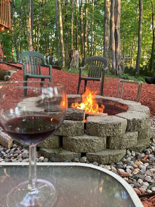 A glass of red wine on a table with a fire pit in the background.