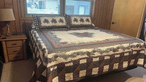 A bedroom with a large bed, a nightstand, a lamp, and a window with blinds.