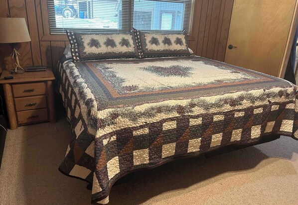 A bedroom with a large bed, a nightstand, a lamp, and a window with blinds.