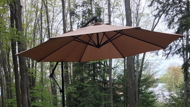 A wooden deck with a table and two chairs, an umbrella, and a forested background.
