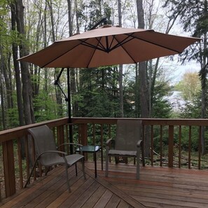 A wooden deck with a table and two chairs, an umbrella, and a forested background.
