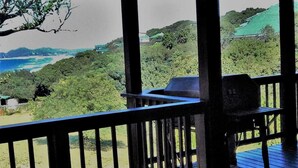 A covered outdoor area with a wooden deck, a table, and a chair. - Alfies House (Ponta d'Ouro)