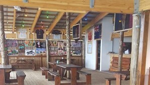 An indoor wooden deck with picnic tables and benches, surrounded by walls with various posters and signs. - Alfies House (Ponta d'Ouro)