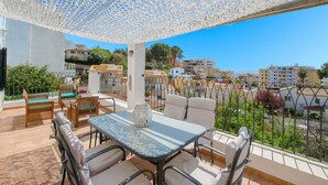 A terrace with a table and chairs, a decorative canopy, and a view of buildings and greenery.