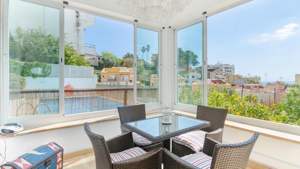 A balcony with wicker furniture, a glass table, and a view of the cityscape.