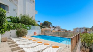 A rooftop pool with white lounge chairs and a lifebuoy.