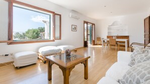 A spacious living room with a large window, a sofa, a dining table, and a kitchen area.