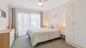 Ein Schlafzimmer mit Bett, Schreibtisch, Stuhl, Kleiderschrank und einem Fenster mit Vorhängen.