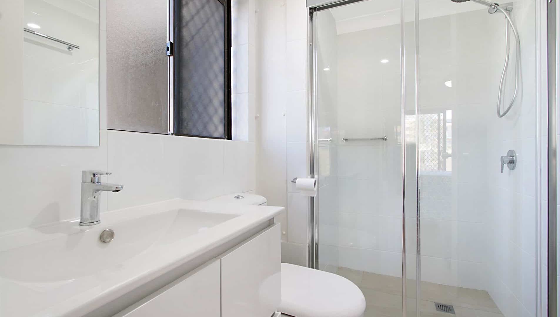 A modern bathroom with a glass shower enclosure, a white sink, and a toilet.