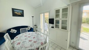 A dining area with a round table, white chairs, a blue sofa, and a cabinet with glass doors. - Agréable pavillon 6 personnes dans résidence avec piscine (009) (Biscarrosse)
