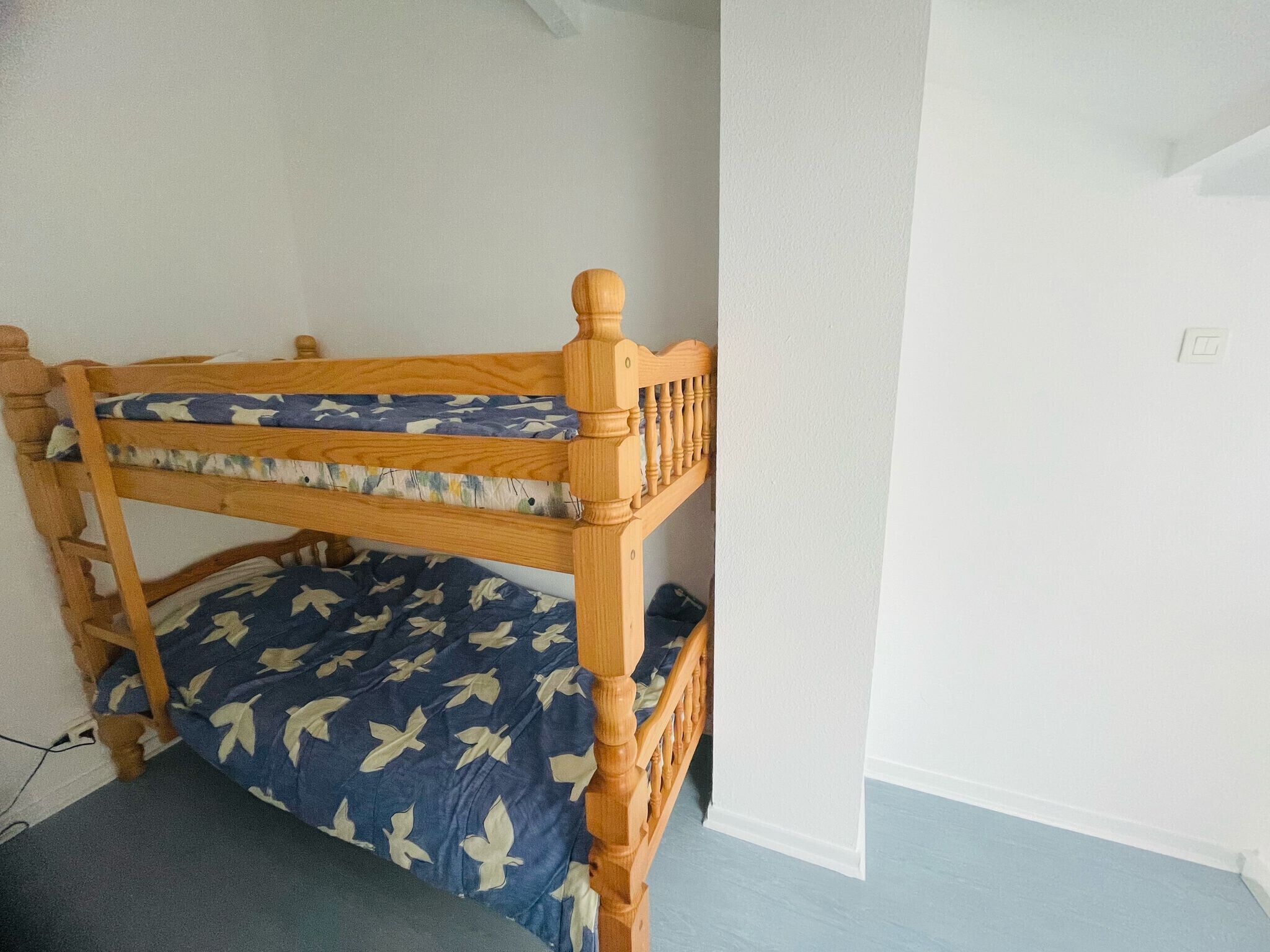 Un lit superposé avec une structure en bois et une literie bleue ornée de motifs blancs.