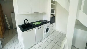 A compact kitchen with white cabinets, a black countertop, a washing machine, and a microwave. - Agréable pavillon 6 personnes dans résidence avec piscine (009) (Biscarrosse)