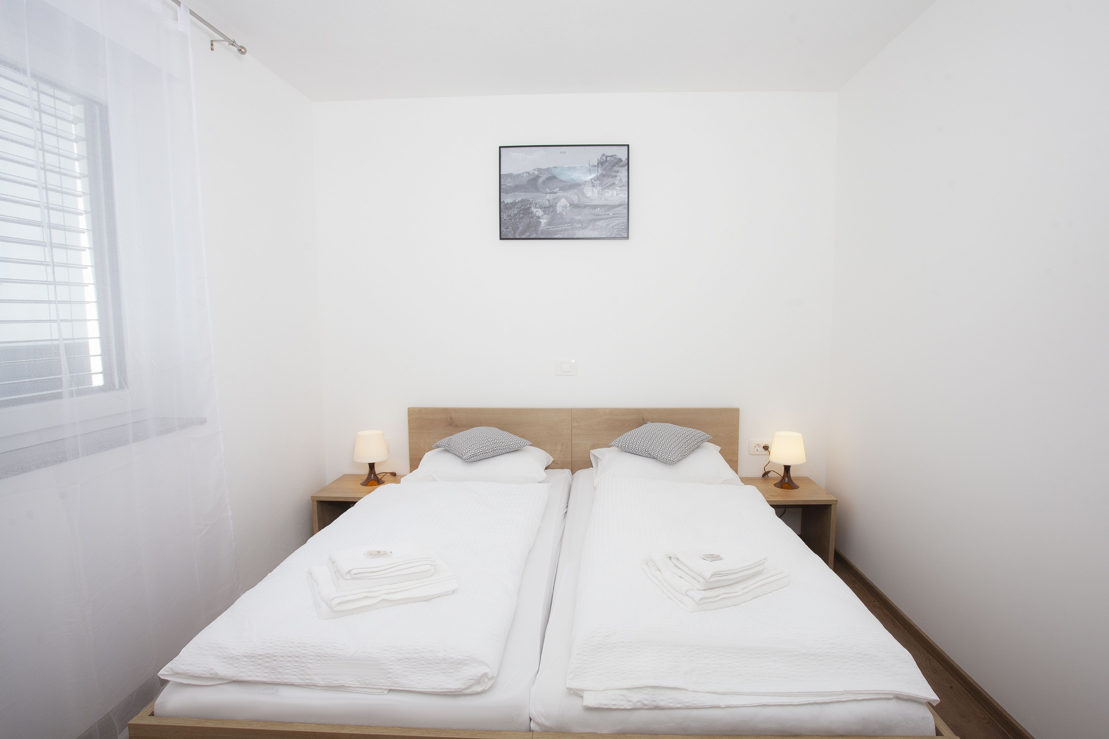 A hotel room with two beds, a window with blinds, a framed picture on the wall, and bedside lamps.