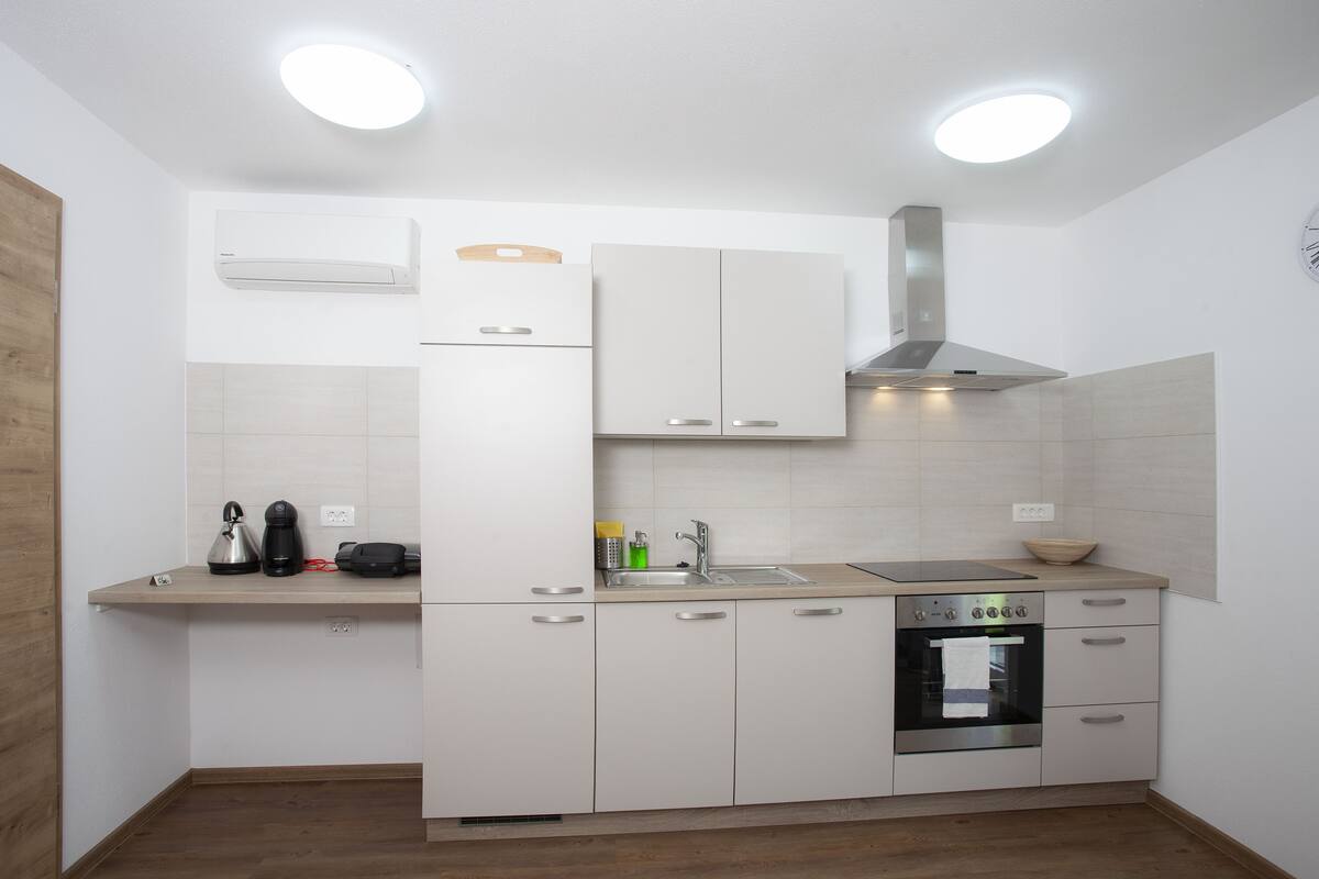 Una cocina moderna con armarios blancos, una campana extractora de acero inoxidable, un horno empotrado y un lavamanos.