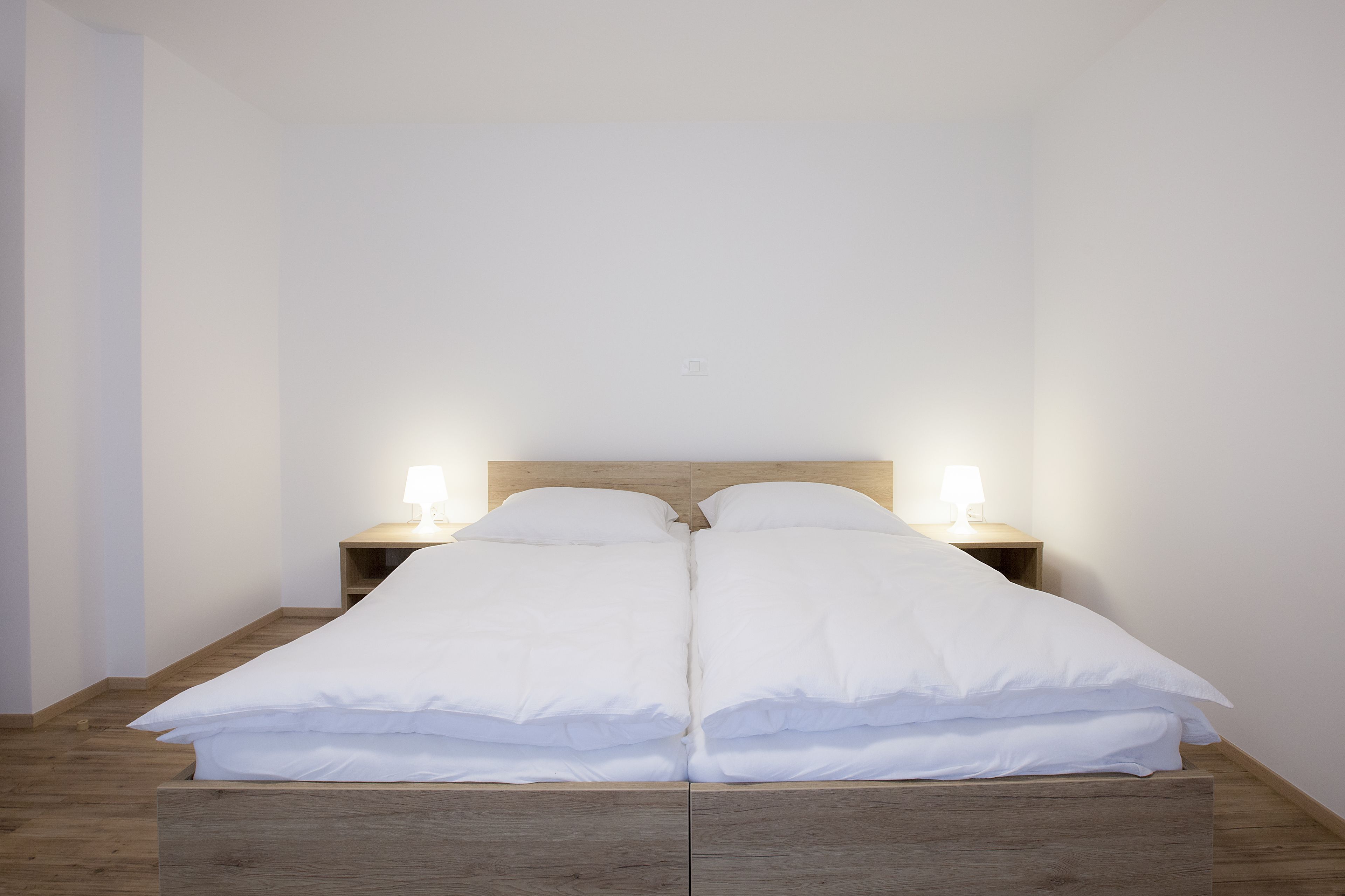 Un lit double avec une literie blanche, deux lampes de chevet et une tête de lit en bois.