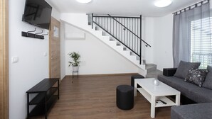 Un salon moderne avec un escalier, un téléviseur à écran plat fixé au mur, un canapé, une table basse et une plante en pot.