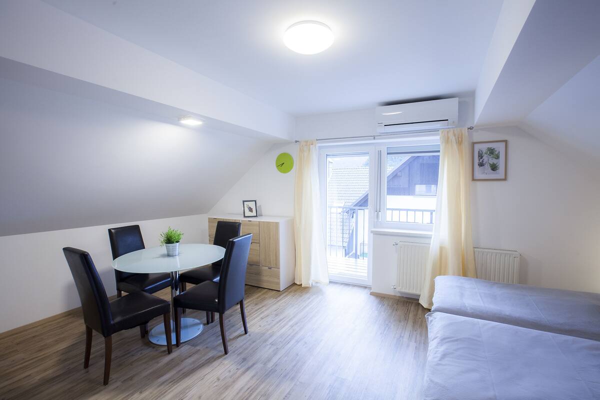 Una habitación moderna y bien iluminada con una mesa de comedor y sillas, una cama y una ventana con cortinas.