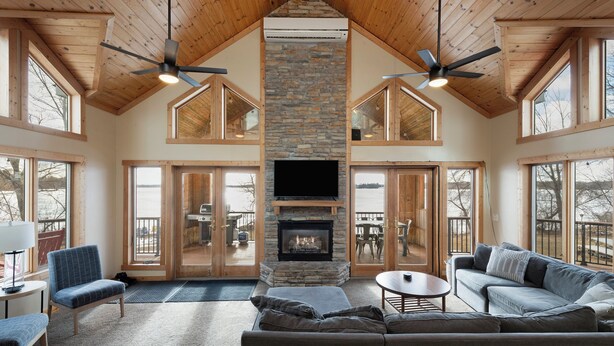 Un salón espacioso con chimenea de piedra, techo de madera y ventanas grandes.