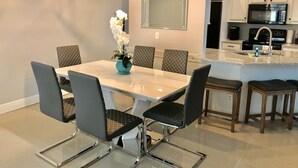 Un comedor con una mesa blanca, seis sillas, un jarrón con flores blancas e iluminación colgante moderna.