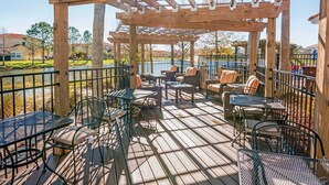 Una terraza de madera con mobiliario exterior, incluyendo sillas y mesas, y una estructura de pérgola.