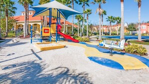 Un parque infantil con tobogán y estructuras para escalar, rodeado de palmeras y un cielo despejado.