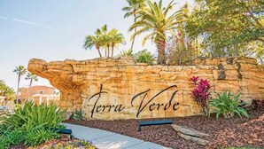 Muro de piedra con el texto "Terra Verde" y jardín paisajístico circundante con diversas plantas y un banco.