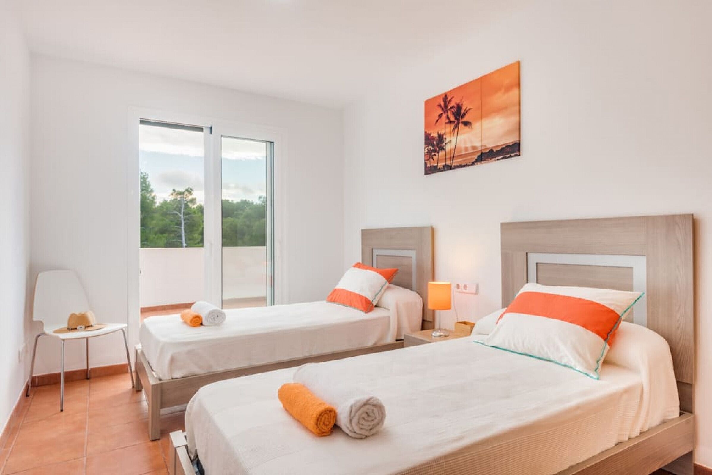Camera d'albergo con due letti, una finestra vista su un'area verde, un quadro appeso al muro e un tavolino con una lampada.