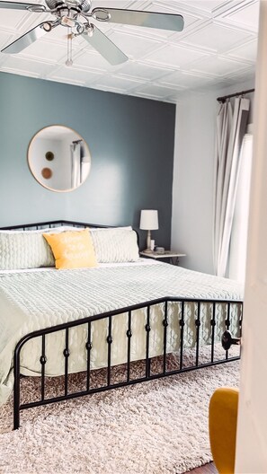 A bedroom with a bed, a round mirror, a nightstand, a lamp, and a ceiling fan.