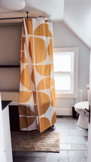 A bathroom with a shower curtain featuring a geometric pattern, a white toilet, and a window providing natural light.