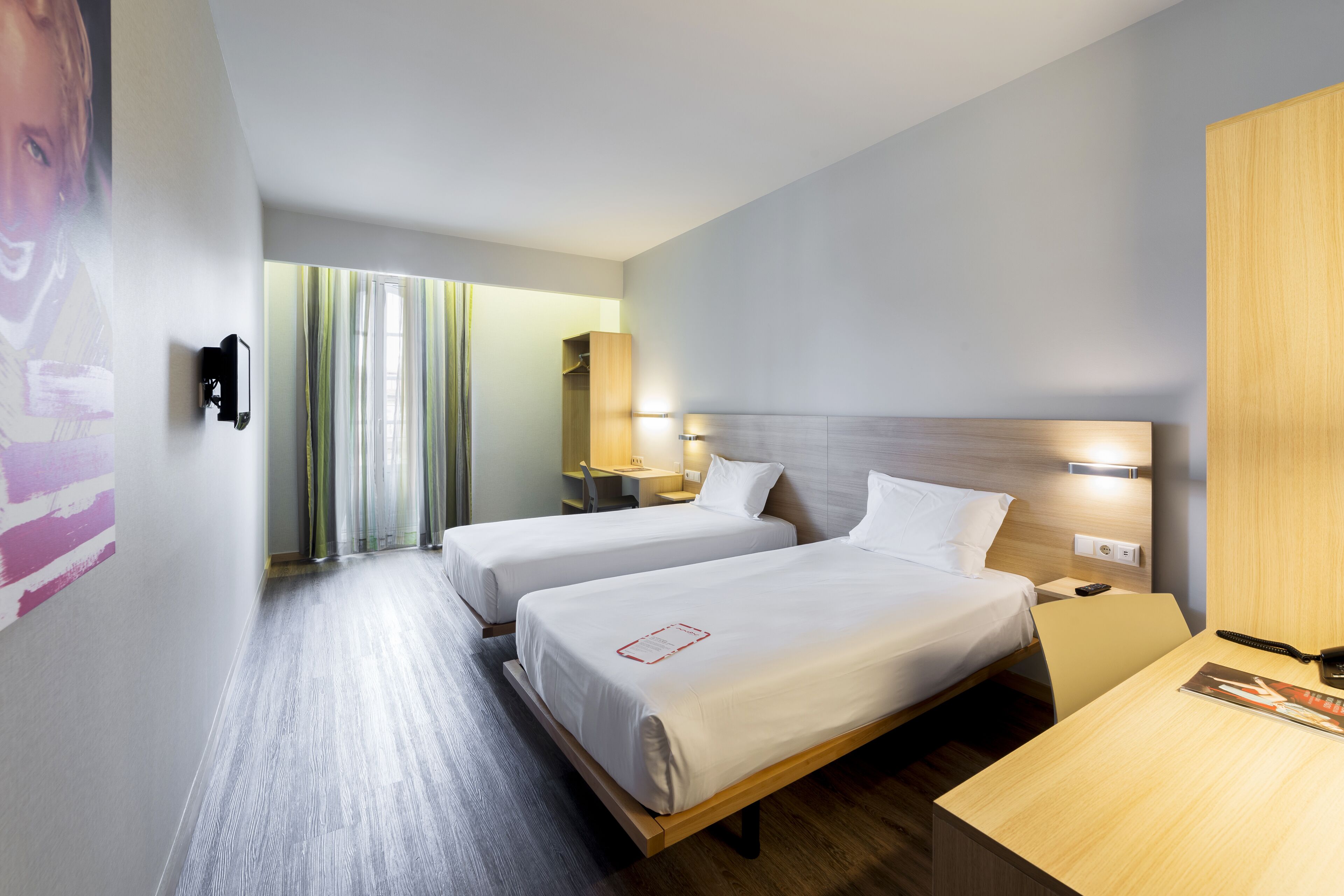 Una habitación de hotel con dos camas, un escritorio, una silla, un espejo y una ventana con cortinas.