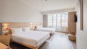 A hotel room with two beds, a desk, a chair, a TV, and a large window. - Moov Hotel Porto Centro (Porto)