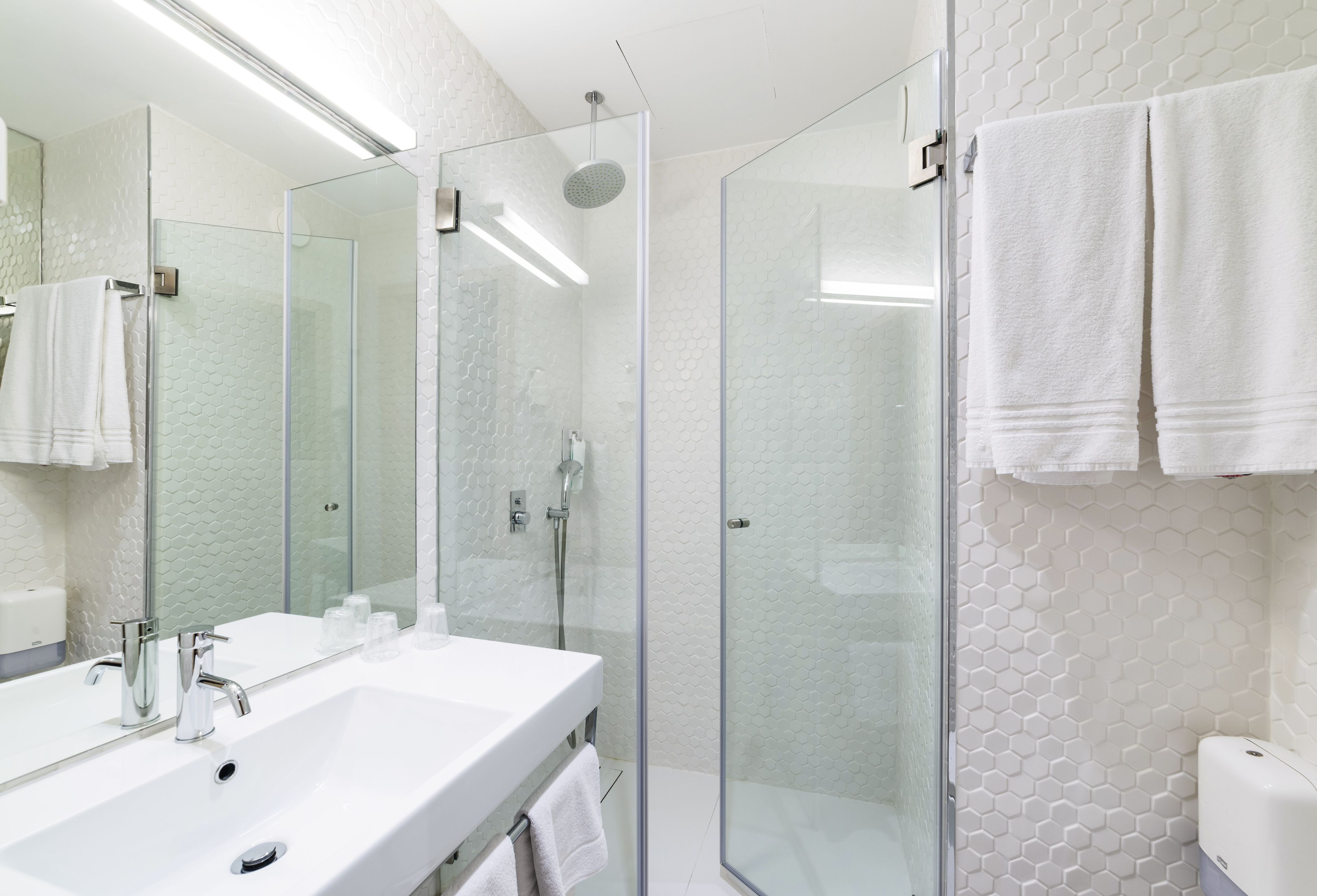 A modern bathroom with a glass-enclosed shower, a white sink, and a large mirror.