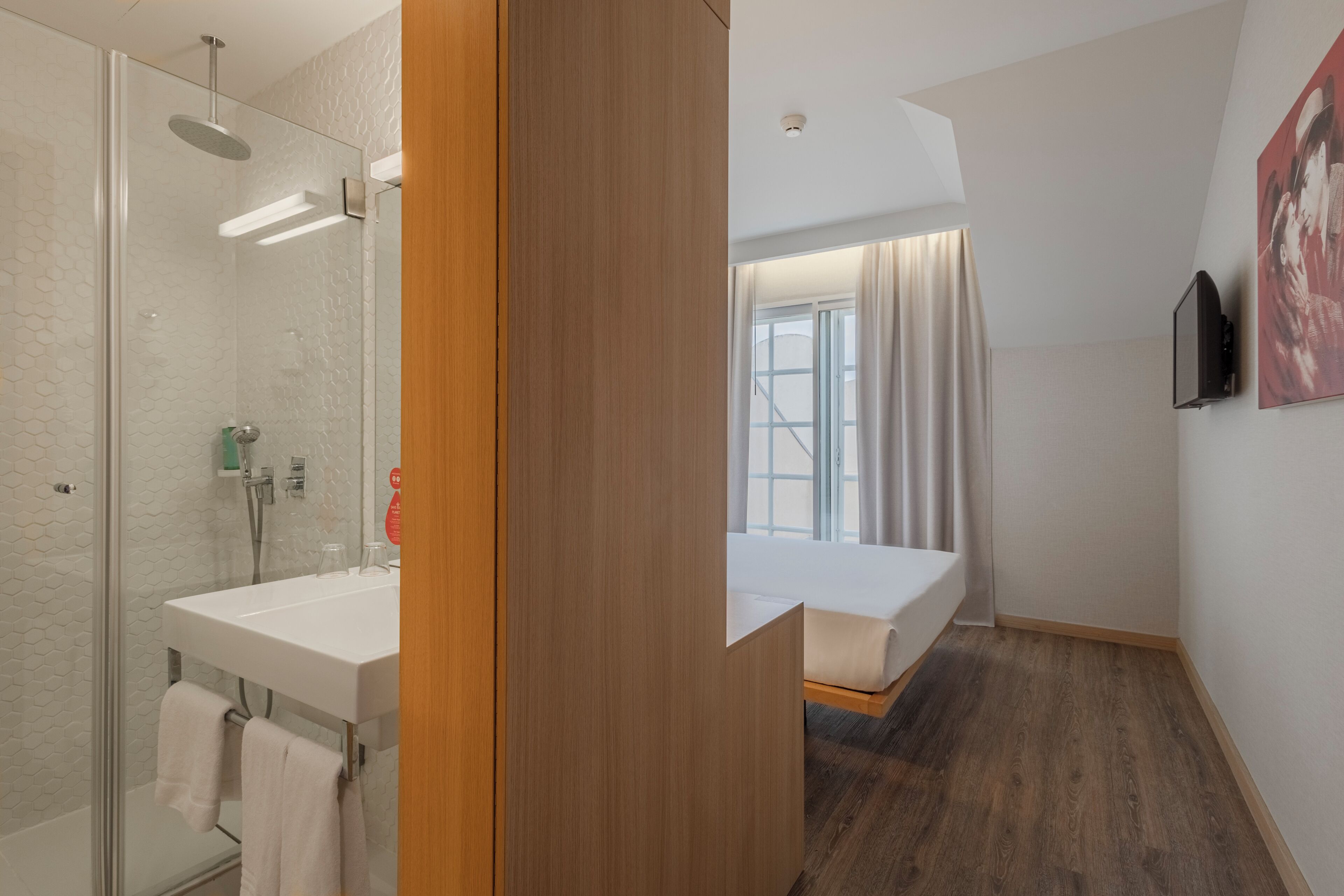 A modern bathroom with a glass shower enclosure, a white sink, and a wooden floor.