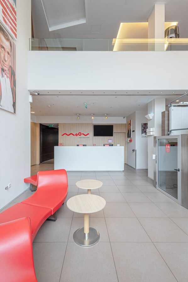 A modern hotel lobby with a reception desk, red seating, and a glass elevator. - Moov Hotel Porto Centro (Porto)