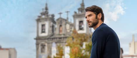 A man standing on a balcony with a clear view of a historic church in the background.
