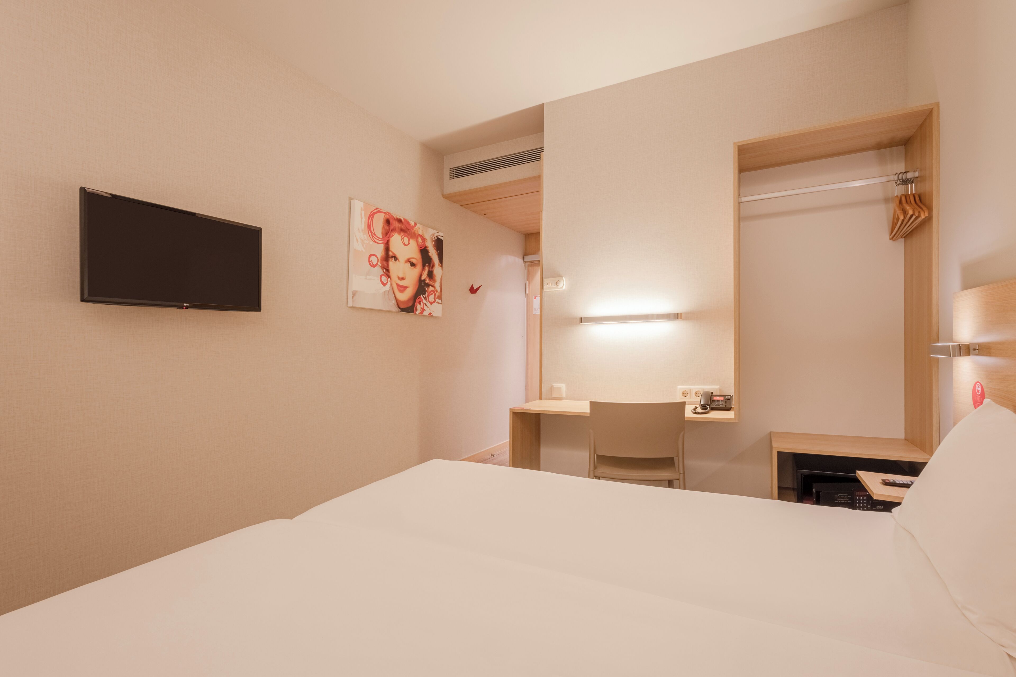 Habitación de hotel con cama, escritorio, silla, televisor de pantalla plana, un cuadro y espejo.