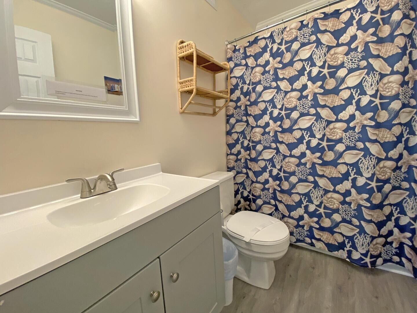 Une salle de bain avec un lavabo blanc, des toilettes et un rideau de douche orné d’un motif de coquillages.