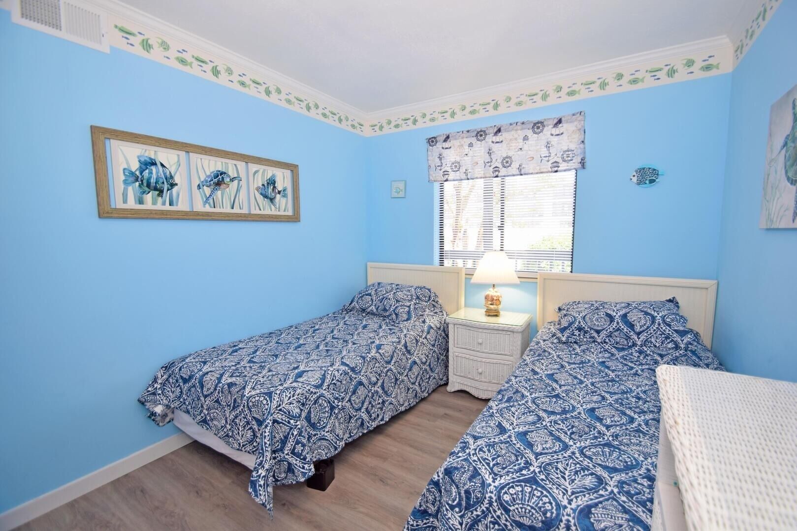 A bedroom with two single beds, a nightstand with a lamp, and a framed picture of fish on the wall.