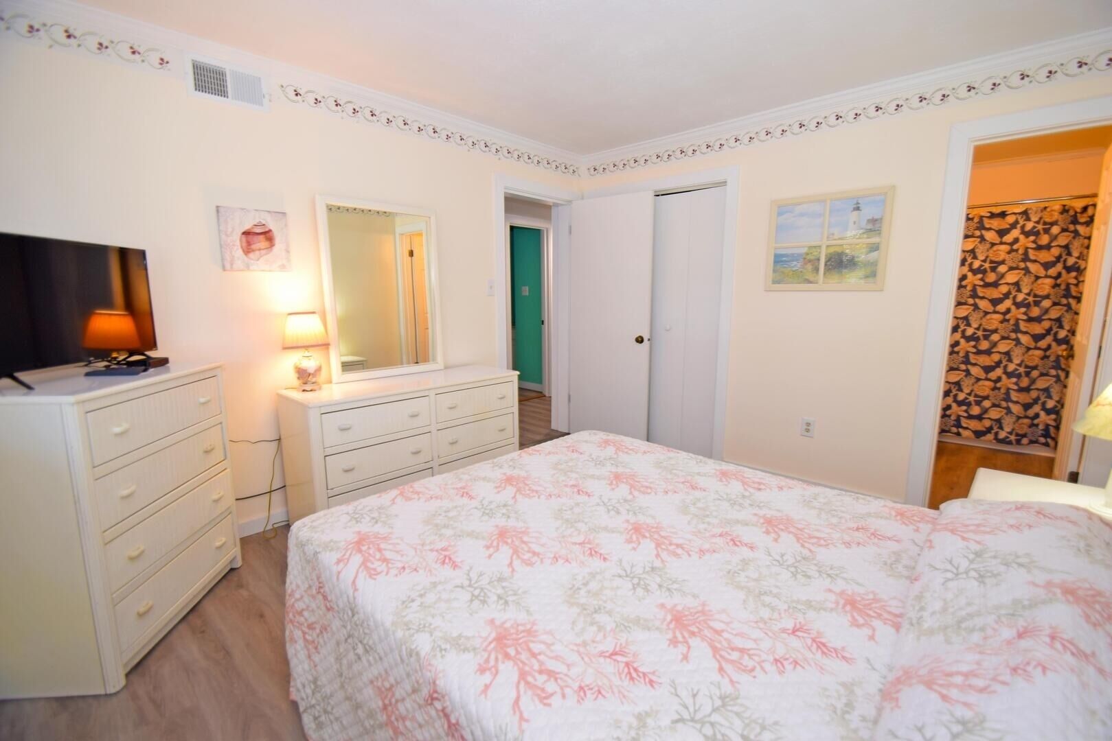 A bedroom with a bed, dresser, TV, and a mirror.