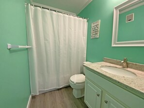 Ein Badezimmer mit weißer Duschvorhang, Toilette, Waschbecken mit Granitplatte und Spiegel.