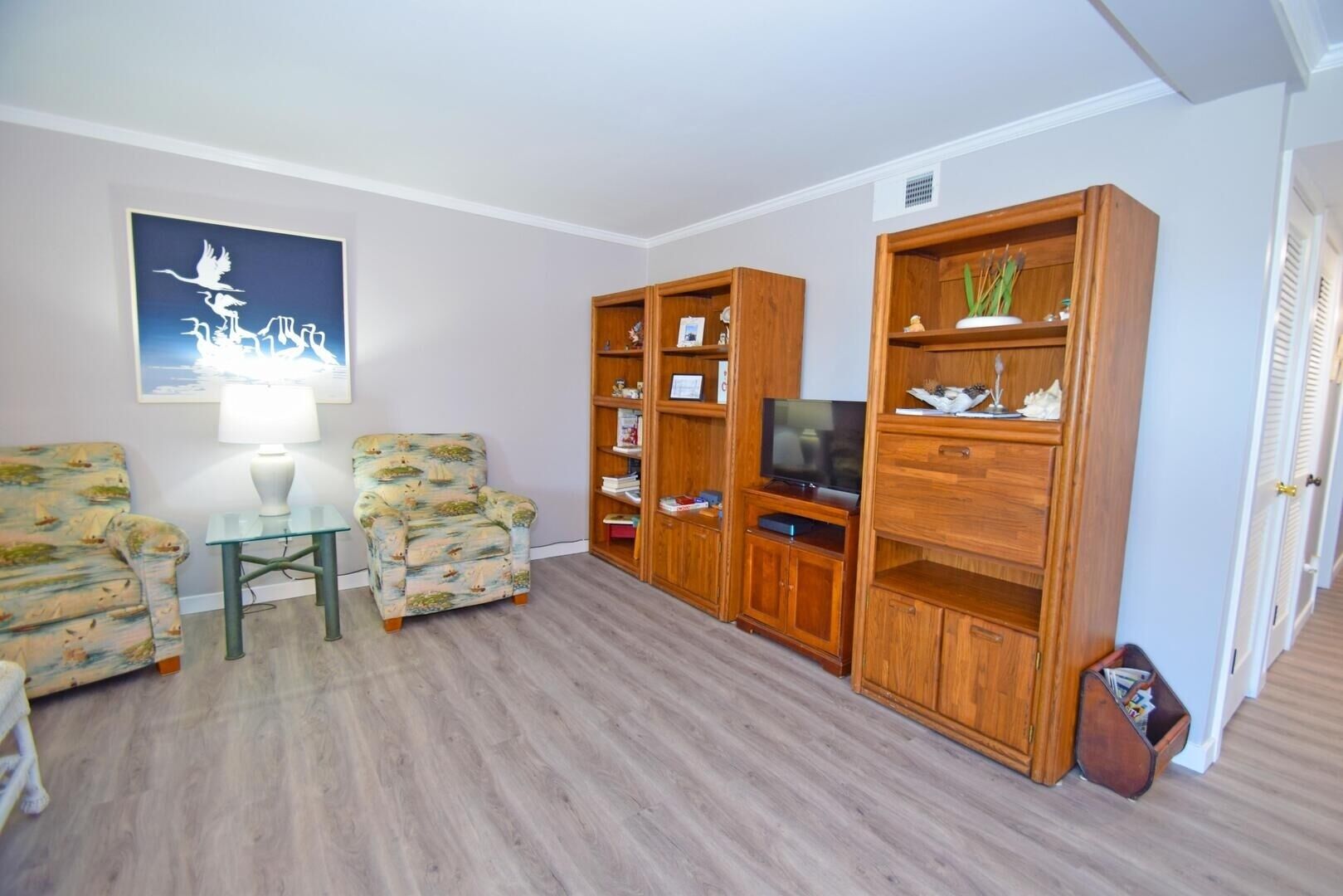 Un salon comprenant deux fauteuils, une table basse en verre, un meuble de rangement en bois avec un téléviseur et un tableau accroché au mur.