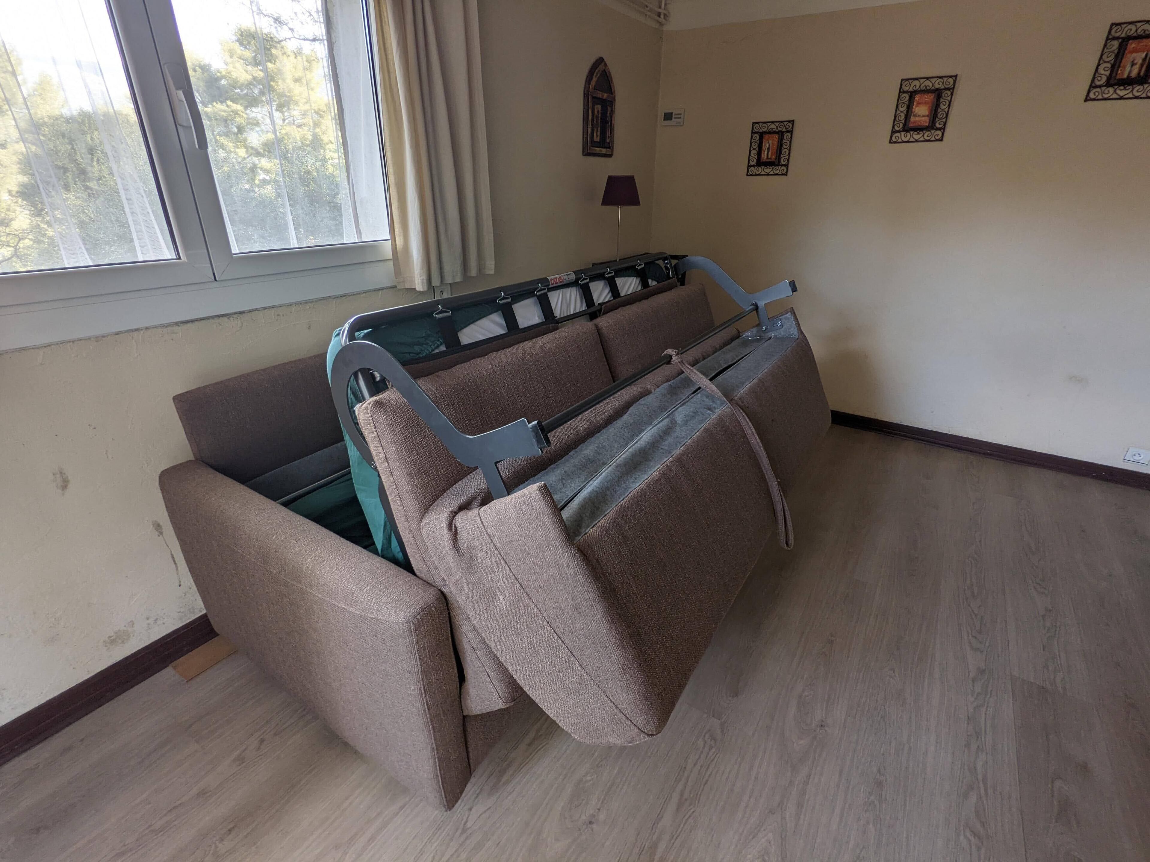 Una habitación con cama, ventana con cortinas, lámpara de pared e imágenes enmarcadas.