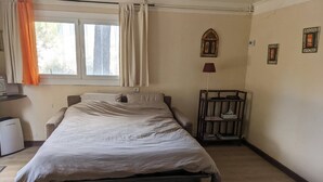 Ein Einzelbett mit Metallgestell, ein Nachttisch mit Lampe sowie ein kleines Regal mit Büchern und einer Taschentuchbox.