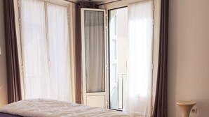 A bedroom with a bed, wooden flooring, a window with curtains, and a small bedside table. - Loft with terrace historic center (Perpignan)