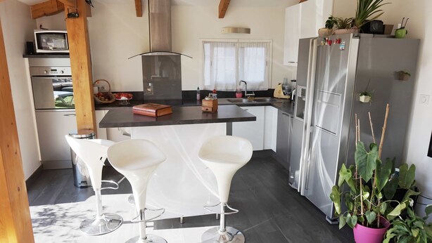 A modern kitchen with a central island, white bar stools, a stainless steel refrigerator, and potted plants. - Loft with terrace historic center (Perpignan)