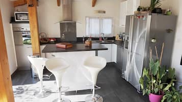Une cuisine moderne dotée d’un îlot central, de tabourets de bar blancs, d’un réfrigérateur en acier inoxydable et de plantes en pot.